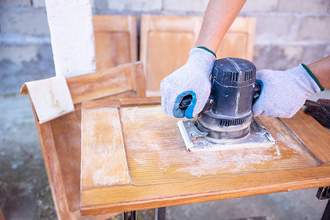 hands using power sander on wood board