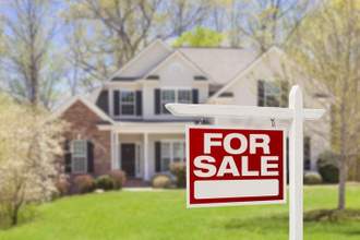 house in the background with a for sale sign in focus in the foreground