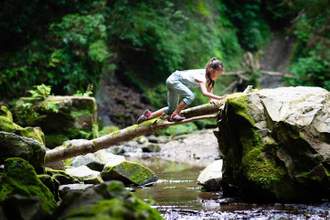 kid climbing up a log to cross a rocky stream
