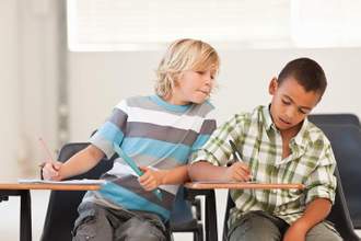 kid leaning over trying to cheat off of his classmate during a test