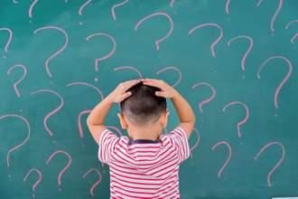 kid with his hands on his head looking at a chalkboard filled with question marks