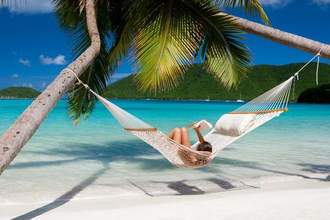 lady laying on a hammock reading a book on the beach
