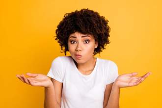 lady with curly hair looking directly at the camera with her shoulders shrugged hands facing upwards looking confused