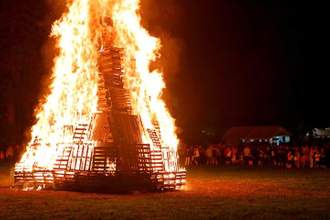large pile of burning crates while a crowd looks on