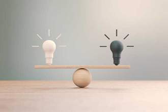 light and dark lightbulbs sitting on a balanced seesaw