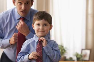 little boy looking into the mirror while his dad teaches him how to tie a tie