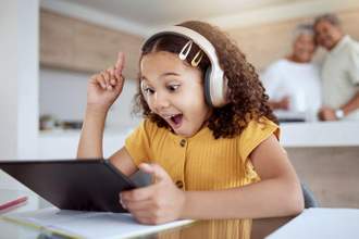 little girl looking excited while listening to something on their tablet