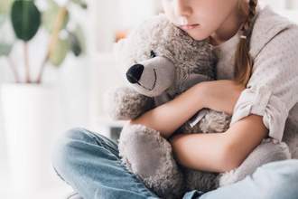 little girl looking worried hugging her stuffed bear for comfort
