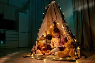 little girl sitting in a fort reading a story to her stuffed animals