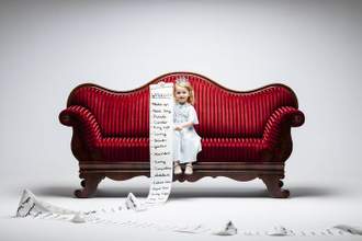 little girl sitting on a large red couch holding a long list to the audience that hits and rolls around the round