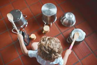 little kid sitting on the kitchen floor banging on pots and pans like a drummer