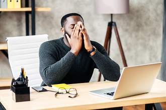 man annoyed at desk with face in hands