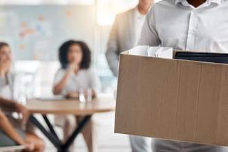 man carrying a box who was fired while his coworker look over in shock