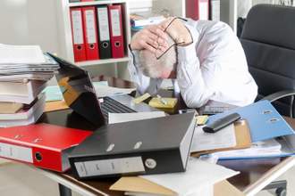 man holding his head in frustration surrounded by paperwork