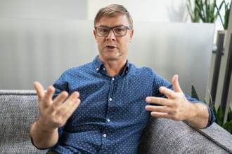 man looking directly at camera speaking with his hands