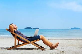 man looking relaxed reclining in his chair on the beach with a laptop in his lap