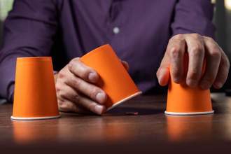 man playing a game of chance trying to find a penny under three cups