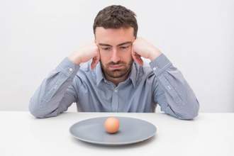 man sitting at a table looking disappointedly at the single hard boiled egg on his plate