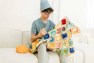 man sitting on couch looking at his crochet project
