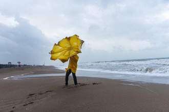 man standing on the beach holding onto his umbrella as it gets picked up by the wind