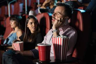man talking loudly on his phone while inside a movie theater