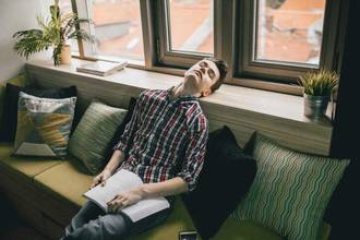 man tilting his head upwards with his eyes closed bored with a book in his lap