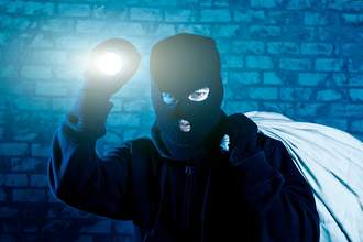 masked man holding a flashlight and a bag over his shoulder