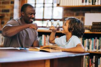 mentor and student giving each other a fist bump in a library