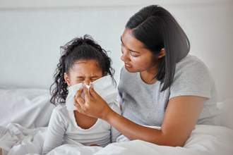 mother holding a tissue up to her sick daughters nose