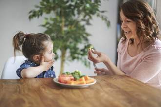 mother trying to get their daughter to eat vegetables