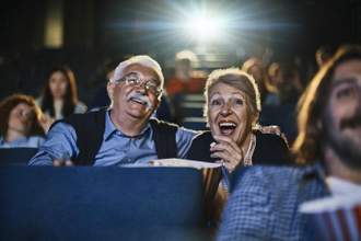 older male and female couple sitting in the movies laughing at what is on the screen in front of them