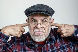 older man plugging his ears and looking angry