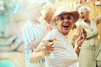 older woman dancing while drinking a glass of white wine looking excited with close friends