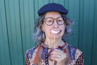 older woman holding up a fake smile in front of her frowning face