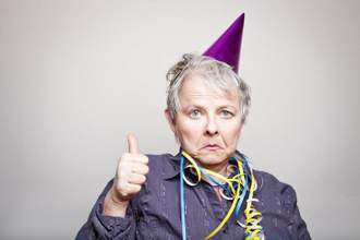 older woman looking glum with birthday hat on giving a thumbs up