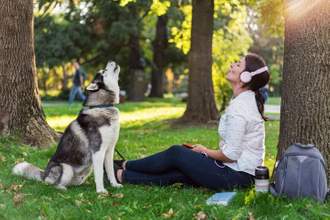 owner and husky sitting in a park howling into the air