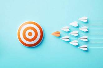 paper planes moving towards a bulls eye target on blue background