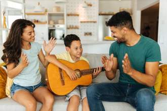 parents sitting on the coach clapping while their child plays the guitar for them