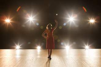 performer standing on stage with a large audience and bright lights