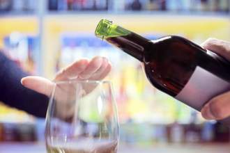 person holding hand over their glass to signify that they no dont want any wine