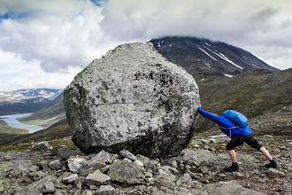 person pushing against large boulder