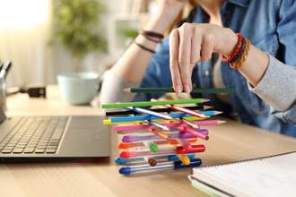 person sitting at their desk cross stacking pens and pencils on top of one another to distract themselves