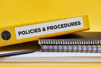 policies and procedures written on the label of a yellow binder on the office desk