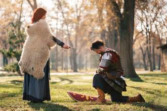 queen using sword for a knighthood ceremony while a knight kneels before her
