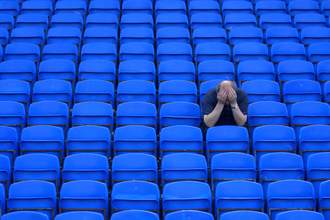 sad fan sits in stands with head in hands