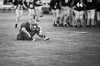 sad football player sitting as other team celebrates