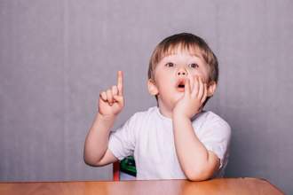 small child sitting at the table waving his finger in the air in an effort to saying something