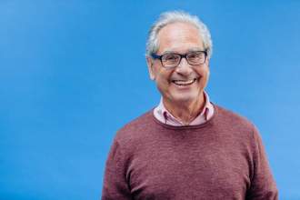 smiling older man standing in front of a blue background