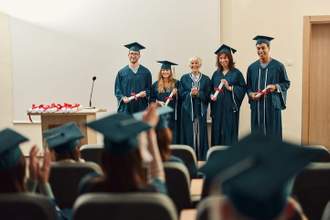 student graduates standing on a stage in front of a crowd receiving their diplomas