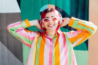 stylish young woman with pink hair and sun glasses in multicolor stripped shirt